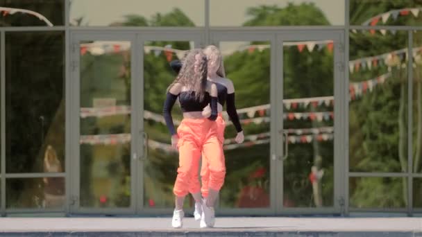 トラックスーツダンスホール ワークの長い髪を持つ2人の若い女性建物の前でストリートモダンダンス ブーティーダンス — ストック動画