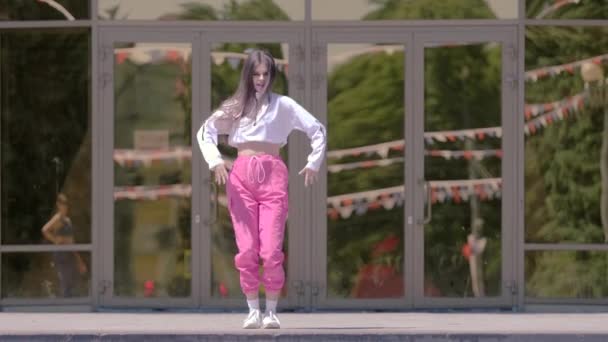 トラックスーツダンスホールのトークで長い髪を持つ若い美しい女の子 屋外でストリートモダンダンス ブーティーダンス スローモーション — ストック動画