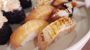 Suşi ve rulo ile tabağa yakın çekim. Restoran mutfağı. Japon yemeği. Kaypak hareket ediyor. Makro görünüm