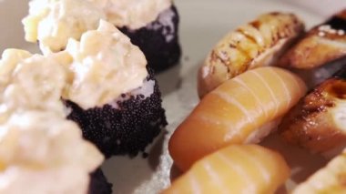 Suşi ve rulo ile tabağa yakın çekim. Restoran mutfağı. Japon yemeği. Kaypak hareket ediyor. Makro görünüm