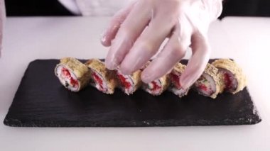 Şefin eldivenli ellerinin bir tabağa suşi koyduğu ön manzara. Restoran mutfağı. Japon yemeği.