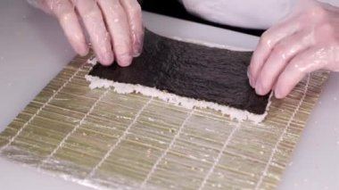 Suşi şefi bambu hasırı kullanarak rulo hazırlıyor. Suşi ustası suşi yapıyor. Suşi ustası, Norveç 'e pirinç döker. Restoran mutfağı. Japon yemeği.