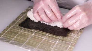 Suşi şefi bambu hasırı kullanarak rulo hazırlıyor. Suşi ustası suşi yapıyor. Suşi ustası, Norveç 'e pirinç döker. Restoran mutfağı. Japon yemeği.