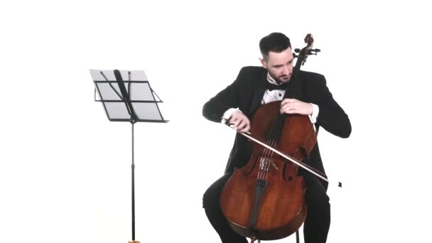 穿着燕尾服的年轻音乐家熟练地在大提琴的音符上演奏缓慢的旋律 交响乐音乐会 被隔离了 — 图库视频影像