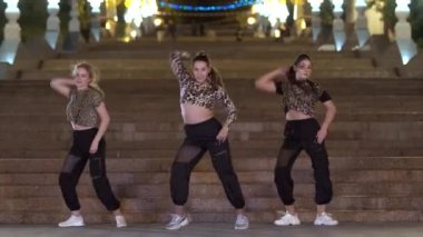 Leopar tişörtlü üç genç kadın akşamları eski büyük taş bir merdivenin önünde dans edip modern danslar ediyorlar.