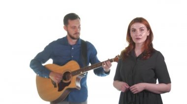 Genç müzisyenlerin düeti. Sakallı bir adam akustik gitar çalar, kızıl saçlı bir kadın şarkı söyler. Beyaz arka plan. İzole edilmiş