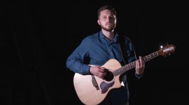 Sakallı yakışıklı yetenekli adam akustik gitar çalıyor. Siyah arka plan. İzole edilmiş