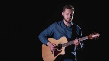 Orta boy, sakallı, akustik gitar çalan yakışıklı bir gitarist. Siyah arka plan. İzole edilmiş