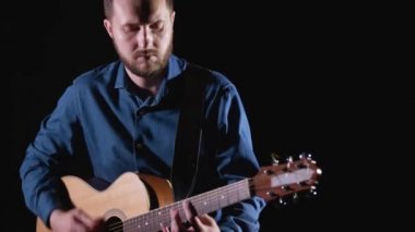 Sakallı yakışıklı yetenekli adam akustik gitar çalıyor. Siyah arka plan. İzole edilmiş