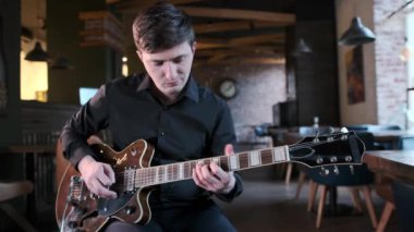 Siyah gömlekli yakışıklı adam kafede gitar çalıyor. Güzel bir blues kompozisyonu. Retro stüdyo, tuğla döşeme. Caz, Blues, Funk. Orta uzunlukta.