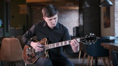 Siyah gömlekli yakışıklı adam kafede gitar çalıyor. Güzel bir blues kompozisyonu. Retro stüdyo, tuğla döşeme. Orta uzunlukta.