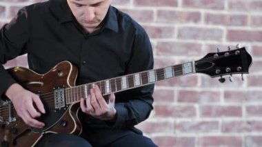 Siyah tişörtlü genç müzisyen caz çalıyor, gitarda blues çalıyor, duvarın arkasında. Caz, Blues, Funk. Orta uzunlukta.