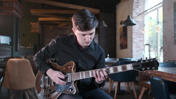 黒シャツのハンサムな男はカフェでギターの美しいブルースの組成物で遊んでいる レトロなスタジオ レンガのインテリア ジャズ ブルース ファンク 中ロングショット — ストック動画