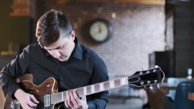 Siyah tişörtlü genç gitarist bir barda blues müzikali icra ediyor. Retro stüdyo, tuğla döşeme. Caz, Blues, Funk. Yakın çekim.