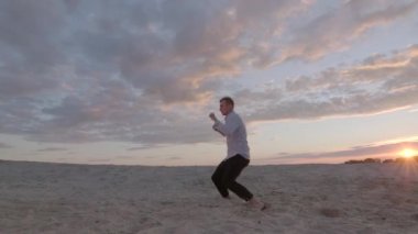 Yakışıklı dansçı gün batımında kumlu plajda serbest dans kompozisyonu sergiliyor. Çağdaş koreografi. Duygular. Yavaş çekim. Dinamik kamera hareketi