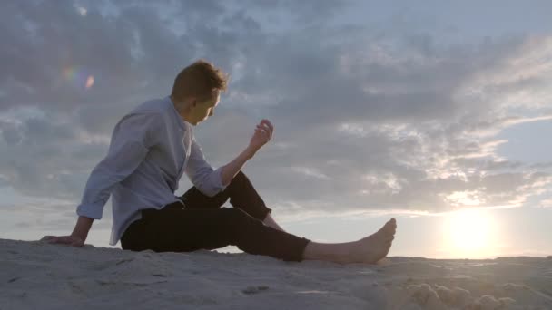 Pensive Blond Man Sits Sand Backdrop Sunset Sky Man Pouring — Stock Video