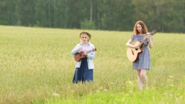 İki güzel kadın gün batımında yeşil bir ormanın arka planında yol boyunca yürüyorlar. Gitar ve ukulele ile country müzik çalmak