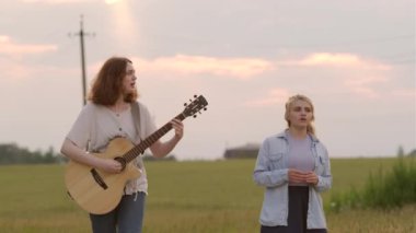 İki güzel genç kız bir yaz akşamında gün batımında bir buğday tarlası boyunca yürür ve şarkı söyler. Kız gitara eşlik ediyor.