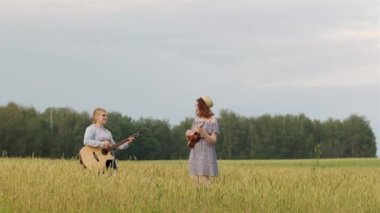 Gitar ve ukulele çalan iki tatlı kızın düeti. Bir yaz akşamında gün batımında buğday tarlası