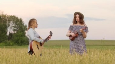 Gitar ve ukulele çalan iki tatlı kızın düeti. Bir yaz akşamında gün batımında buğday tarlası