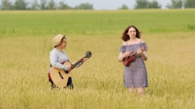 Gitar ve ukulele çalan iki tatlı kızın düeti. Bir yaz akşamında gün batımında buğday tarlası
