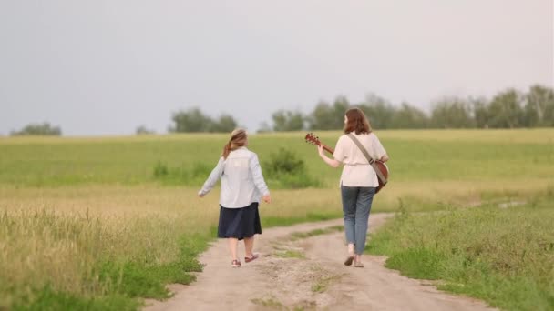 Two Young Girls Guitar Ukulele Walking Road Wheat Field Sunset — Stock Video