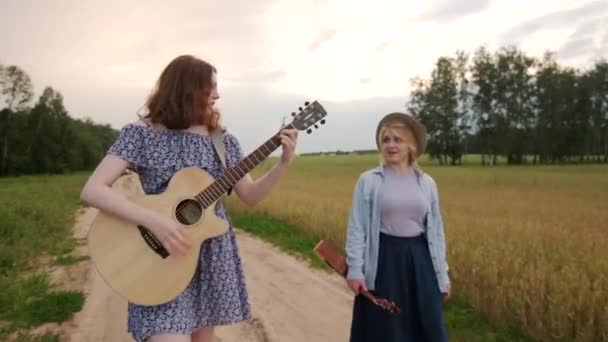 Две Молодые Женщины Ходят Поют Вдоль Дороги Вдоль Пшеничного Поля — стоковое видео