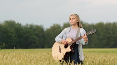 Güzel genç bir kadın buğday tarlasında gitar çalıp şarkı söylüyor. Güzel bir yaz akşamı.