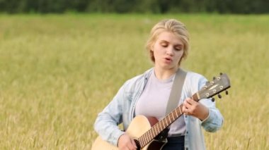 Genç bir kız güzel bir yaz akşamında gün batımında bir buğday tarlasında gitar çalıp şarkı söylüyor.