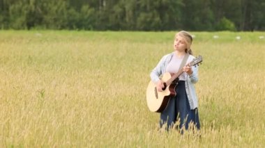 Genç bir kız güzel bir yaz akşamında gün batımında bir buğday tarlasında gitar çalıp şarkı söylüyor.