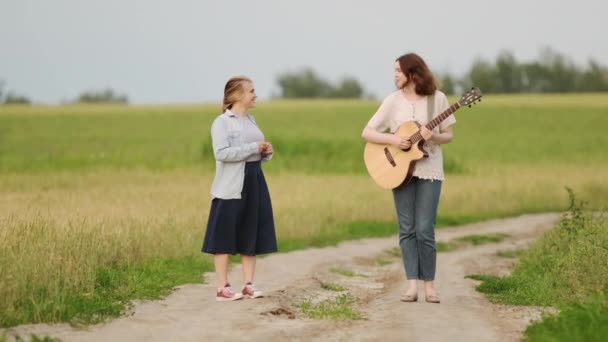 傍晚时分 两个漂亮的女人站在麦田里的路上 带着吉他的女孩慢动作 — 图库视频影像