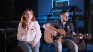 Bir gitarist düeti ve bir müzik stüdyosunda kızıl saçlı bir şarkıcı. Orta uzunlukta.