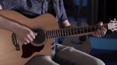 Sakallı bir adam bir müzik stüdyosunda akustik gitar çalar. Gitar telleri ve boyuna yakın çekim.