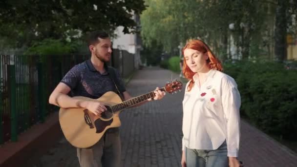 Man Med Skägg Spelar Akustisk Gitarr Rödhårig Kvinna Sjunger Stadsparken — Stockvideo