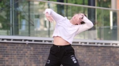 Genç dansçı kız binanın arka planında hip hop dansı yapıyor. Modern gençlik dansının olağanüstü unsurlarını sergiliyor.