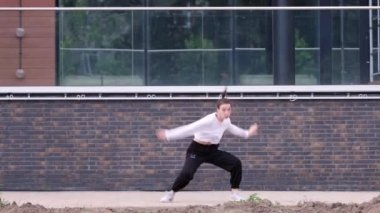 Hip hop koreografisi yapan ve binanın arka planında break dans yapan genç bir kadının videosu. Yavaş çekim