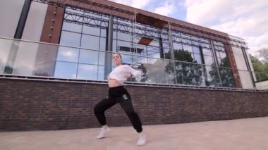 Genç dansçı kız binanın arka planında hip hop dansı yapıyor. Modern gençlik dansının olağanüstü unsurlarını sergiliyor. Gimbal atışı.