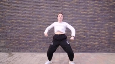 Aktif genç bir kadının hip hop koreografisi ve açık havada duvarın karşısında dans edişinin videosu. Ağır çekim. Gimbal atışı.