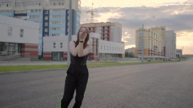 Geniş bir caddede dans eden genç ve güzel bir kadın. Yaz akşamı. Güneşli gün batımı. Hip hop. Çağdaş koreografi. Ağır çekim. Gimbal atışı.
