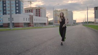 Geniş bir caddede dans eden genç ve güzel bir kadın. Yaz akşamı. Güneşli gün batımı. Hip hop. Çağdaş koreografi. Ağır çekim. Gimbal atışı.