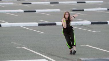 Uzun saçlı neşeli genç bir kadın otoparkta hip hop dansı yapıyor. Modern gençlik dansının olağanüstü unsurlarını sergiliyor. Yavaş çekim