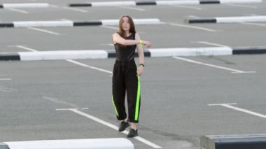 Uzun saçlı genç kız araba parkında serbest dans ediyor. Gülme ve dönme. Sokak dansı. Yavaş çekim
