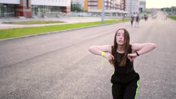 活動中の若い女性がヒップホップ振付を踊ったり 広い街の通りでダンスを壊したりする映像 夏の夜 晴れた日没 スローモーション 手カメラ — ストック動画