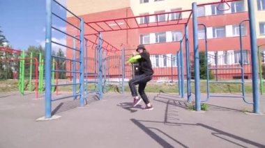 Sportsground 'da eşofmanlı ve şapka dansı yapan neşeli genç bir kadın. Şehirde serbest dans yapan bir şehir. Gençlik alt kültürü