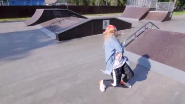 Kırmızı bandanalı genç bir kadın hip hop koreografisi yapıyor ve kaykay alanında break dans yapıyor. Yavaş çekim