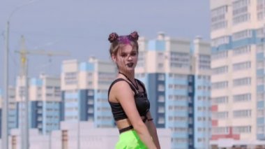 Yüksek binaların arka planında dans eden genç ve güzel bir kadın neşeyle zıplıyor ve kameraya bakıyor. Yavaş çekim