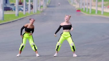 Çıplak omuzlu, açık havada dans eden, sokak dansı yapan, geniş bir sokakta hip hop koreografisi yapan iki genç ve neşeli kadın. Yavaş çekim