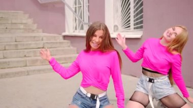Merdiveni olan bir binanın önünde kısa şortla dans eden genç ve neşeli kızların düeti. Yavaş çekim