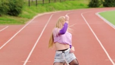 Stadyum koşu bandında dans eden genç ve güzel bir sarışın. Kalçalarını hareket ettiriyor. Yavaş çekim