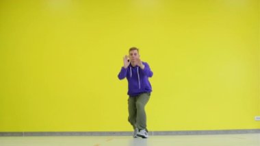 Sarı duvar arkasında hip hop dansı yapan genç bir adam. İzole edilmiş.